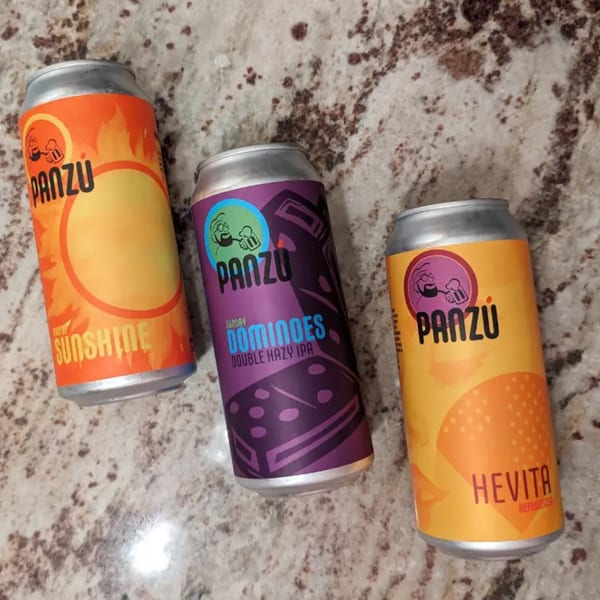 Three colorful Panzu Brewery beer cans, "Sunshine," "Sunday Dominoes," and "Hevita," on a speckled counter.