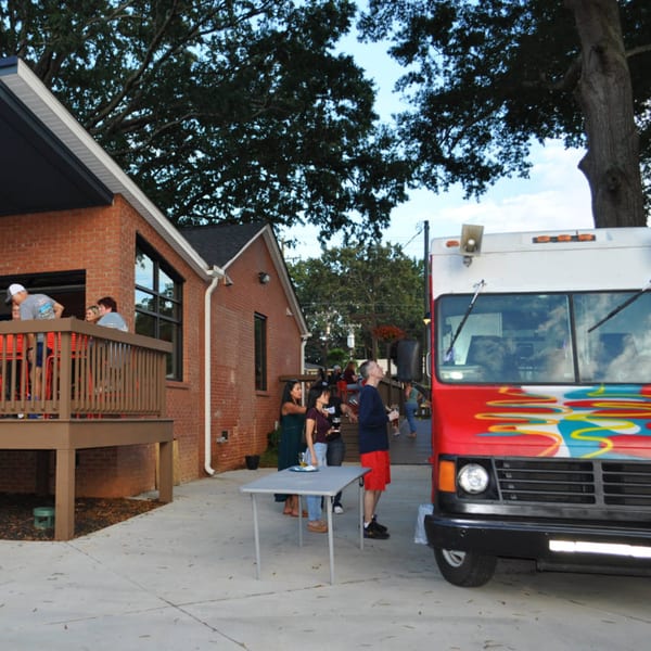 Patrons socialize on a brewery patio and deck next to a colorful food truck.