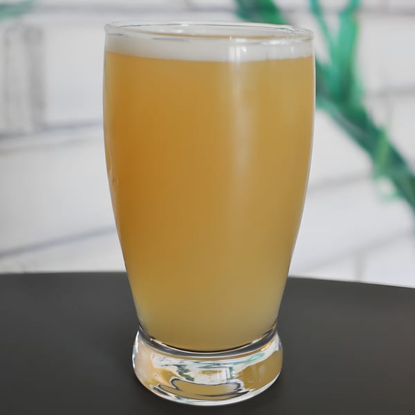 A glass of Panzu Brewery's light-colored beer with a foamy head sits on a dark table.