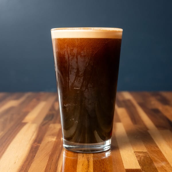 A pint glass of dark beer with a creamy head sits on a wooden table.