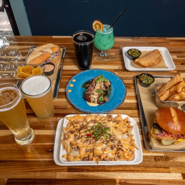 A wooden table laden with various Panzu Brewery dishes, including burgers, fries, and beers.