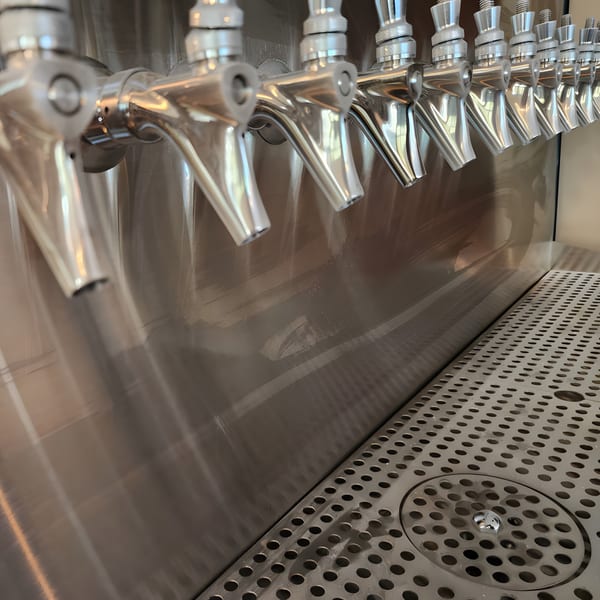 A row of shiny silver beer taps with a drip tray at Panzu Brewery.