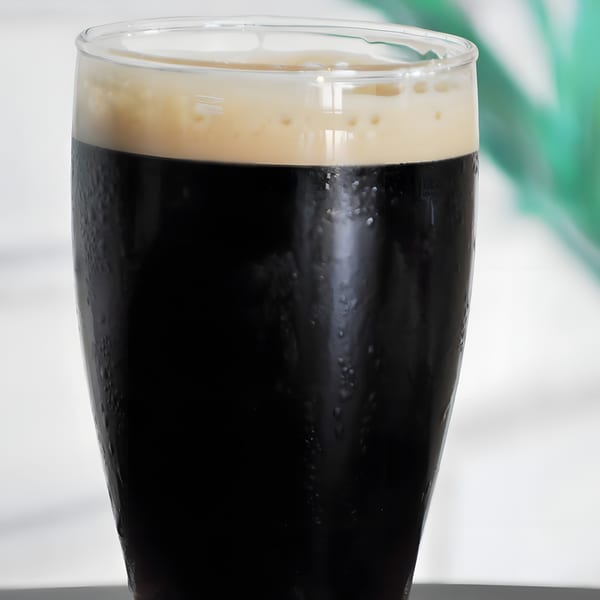 Close-up of a dark stout beer with a creamy head in a glass, condensation on the side.