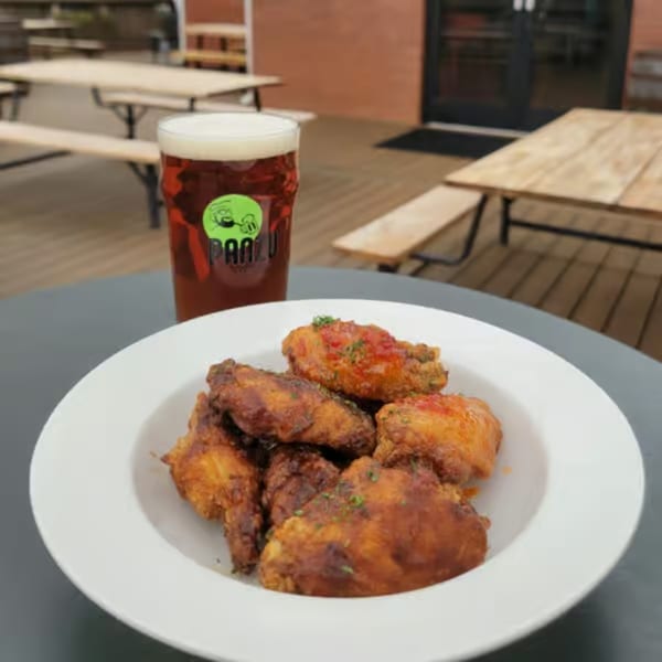 A plate of crispy chicken wings and a pint of Panzu Brewery beer on an outdoor table.