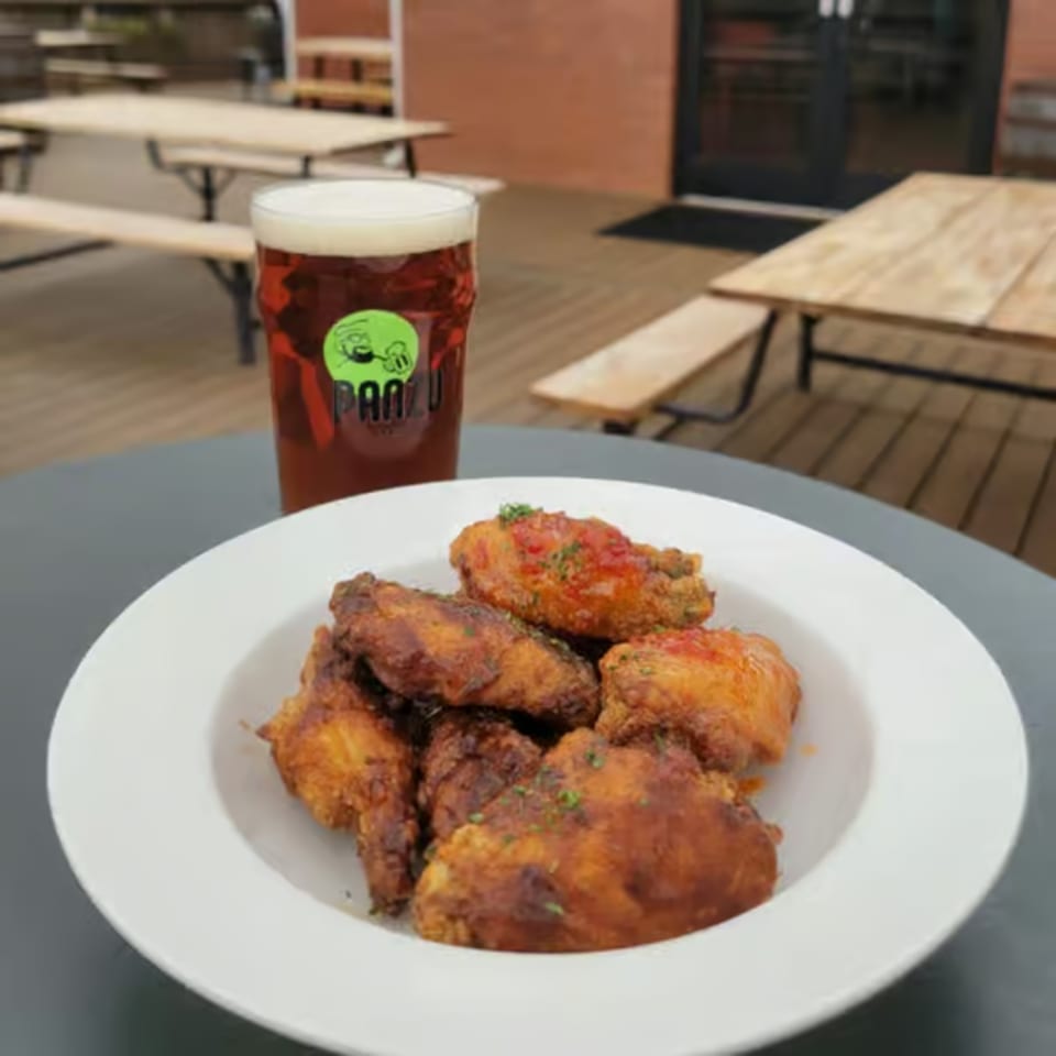 A plate of crispy chicken wings and a pint of Panzu Brewery beer on an outdoor table.
