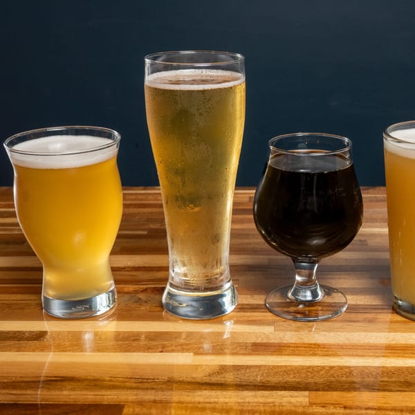 Four glasses of Panzu Brewery beer, including light and dark varieties, on a wooden table.
