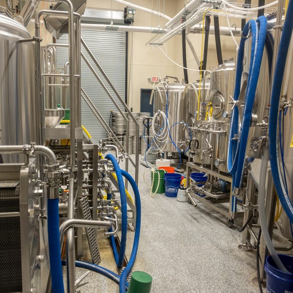 Stainless steel brewing tanks and equipment with blue hoses fill the Panzu Brewery production room.