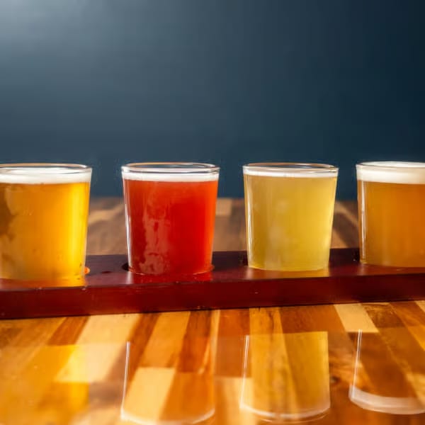 Four beer tasters, two golden, one red, and one pale yellow, on a wooden paddle.