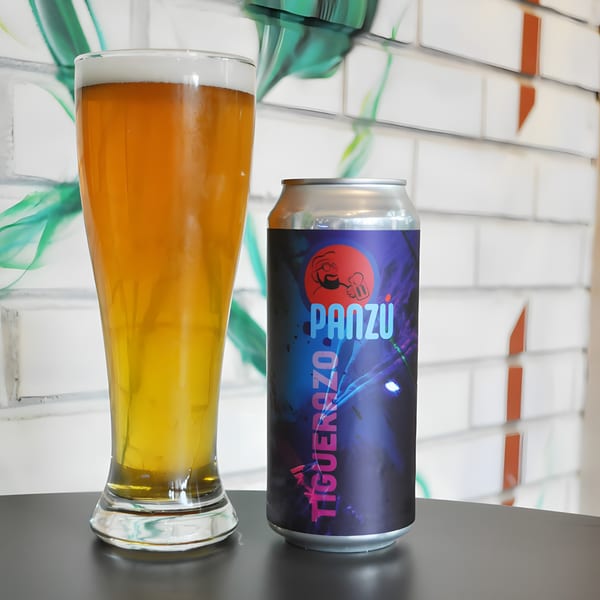 A Panzu Brewery beer can and a glass of golden beer on a dark table.