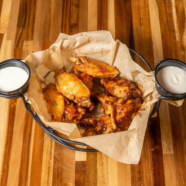 A basket of Panzu Brewery's glazed chicken wings with two dipping sauces on a wooden table.