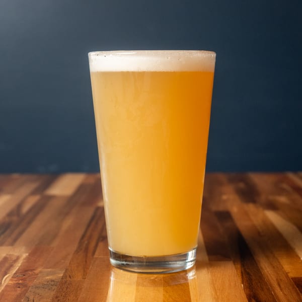 A tall glass of Panzu Brewery's hazy pale ale with a foamy head on a wooden table.