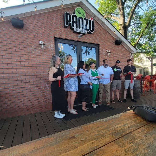 Panzu Brewery's grand opening with a group of people cutting a red ribbon in front of the brick building.