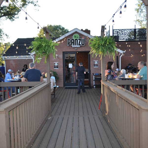 Panzu Brewery's outdoor patio with string lights, hanging plants, and people dining at tables.