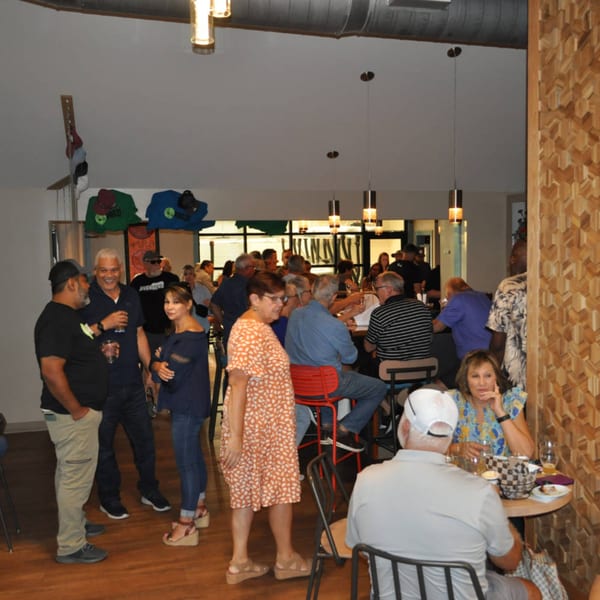 Patrons socialize in the Panzu Brewery, with some standing and others seated at tables and a bar.