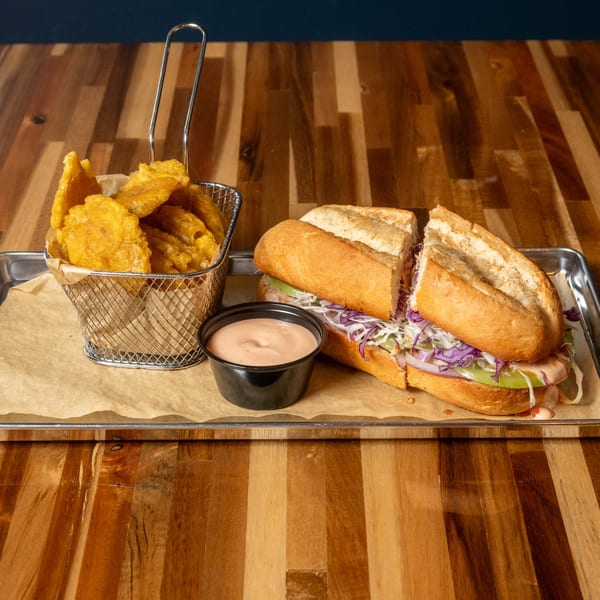 A Panzu Brewery sandwich with purple and white cabbage, and a side of plantain chips and dipping sauce.