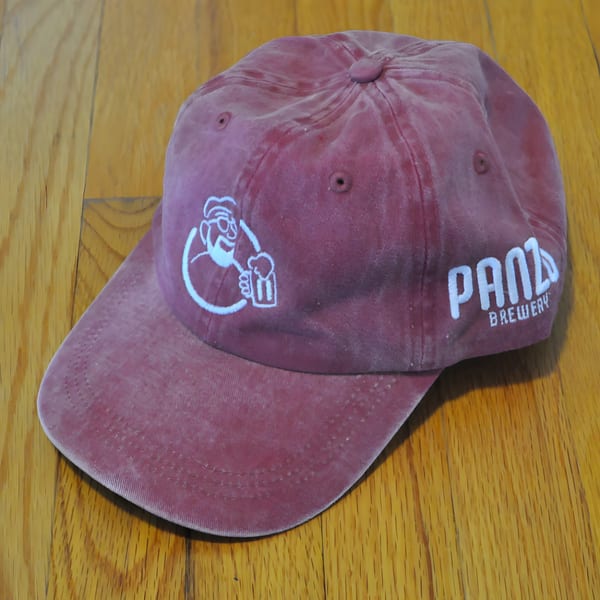 A maroon Panzu Brewery baseball cap with a logo of a man holding a beer.