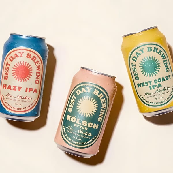 Three cold, non-alcoholic Best Day Brewing cans: Hazy IPA, Kölsch, and West Coast IPA.