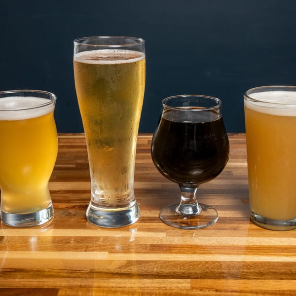 Four glasses of Panzu Brewery beer, including light and dark varieties, on a wooden table.