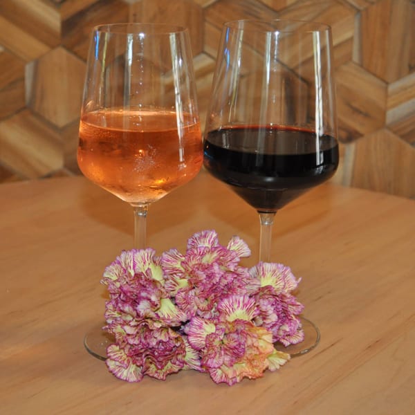 Two wine glasses, one with rosé and one with red wine, sit on a table with purple and yellow flowers.