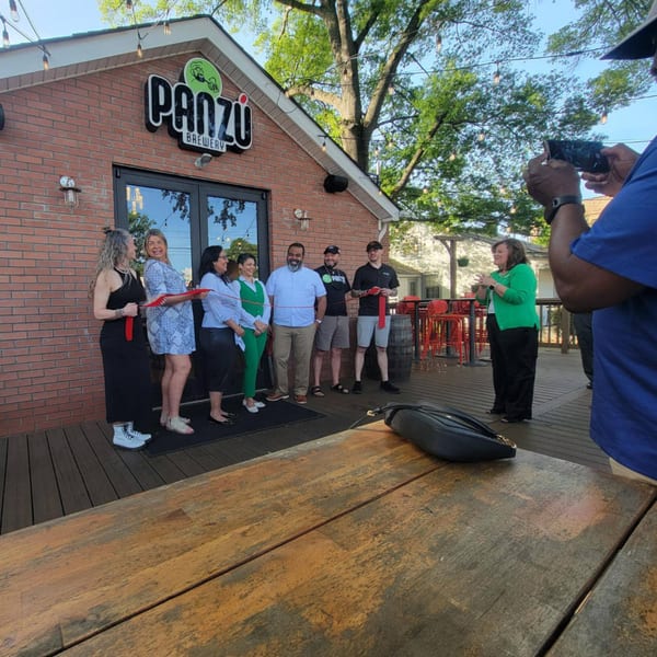 People gathered on a wooden deck in front of Panzu Brewery for a ribbon-cutting ceremony.
